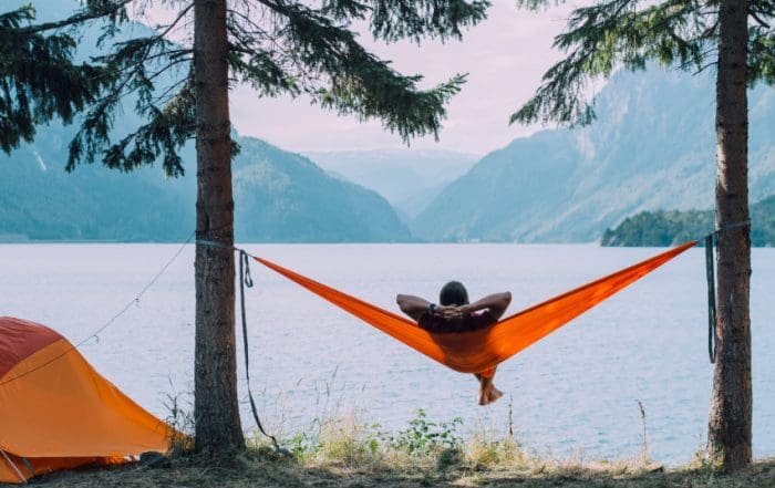 Back view of man silhouette relaxing on orange hammock between two trees pine enjoying the view at the lake in summer norwegian cloudy morning.