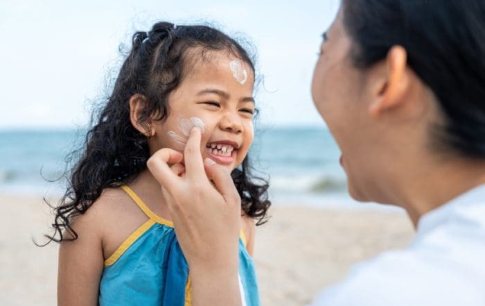 Asian mom applying sunscreen to her happy child’s face on the beach for skin protection from the sun. a young mother carefully smears protective cream on her daughter’s face for safe outdoor fun.